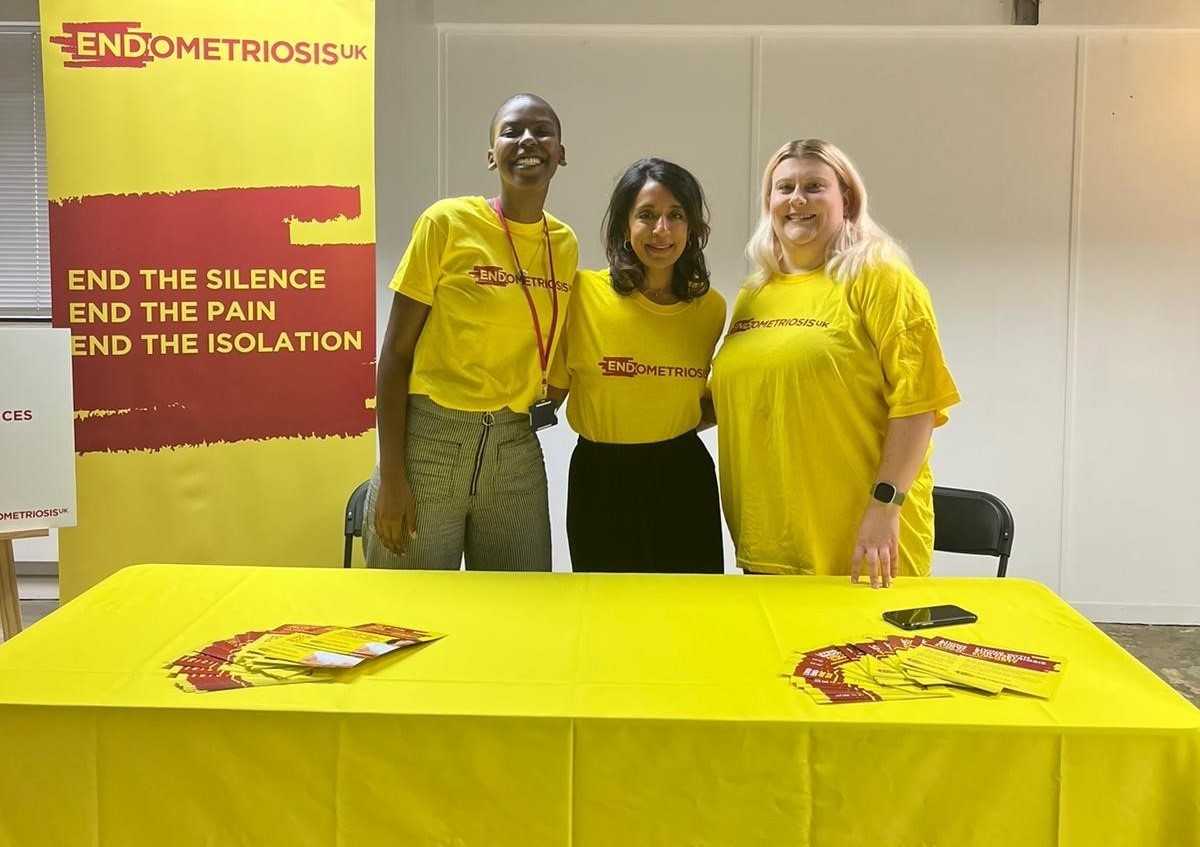 Three volunteers in branded t shirts standing behind brand stand. With branded pop up.