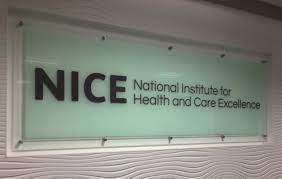 Glass wall sign displaying the NICE logo and name. The sign reads “NICE” in large black letters, followed by “National Institute for Health and Care Excellence” in smaller black text. The sign is mounted with metal fixings against a light-coloured wall with a textured wave pattern.