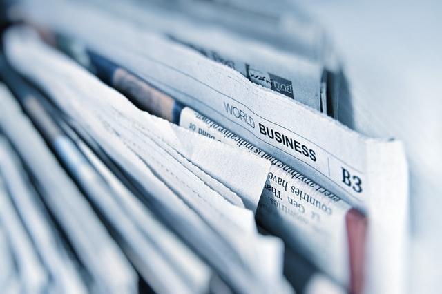 A close-up, shallow-focus shot of a stack of folded newspapers, with one section's "World Business" header and page number "B3" visible in sharp focus, while the rest of the papers fade into a soft blur.