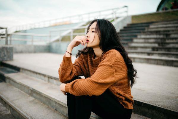 A woman in an orange top sits thinking