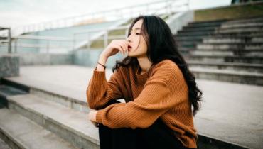 A woman in an orange top sits thinking