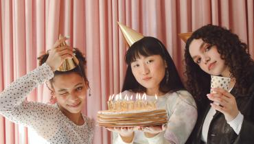 Three people with party hats and a cake