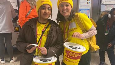 A picture of two of our Bucket Collection volunteers dressed in bright yellow Endometriosis UK hats and t-shirts, holding a yellow bucket each